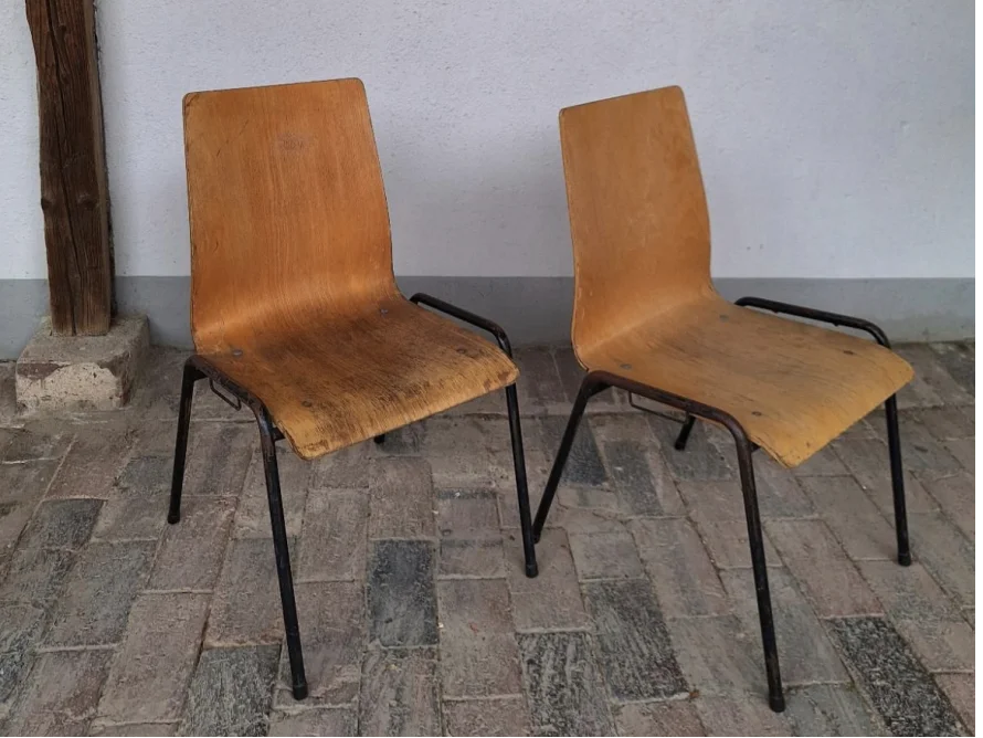 Zwei einfache Stühle mit Holzsitzfläche und schwarzen Metallbeinen