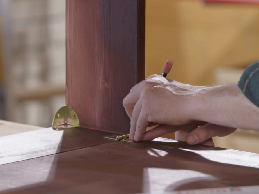 Person befestigt Scharnier an Holz