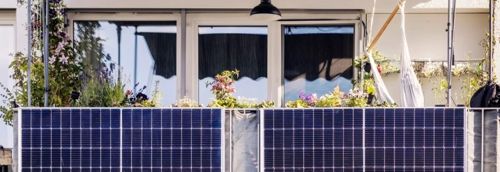 Zwei Solarmodule sind an einem Balkongeländer mit Blumenkästen befestigt.