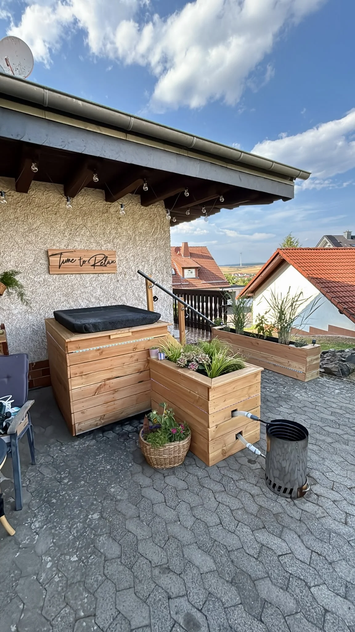 Selbstgebauter Badezuber aus Holz mit externer Heizspirale auf einer Terrasse.