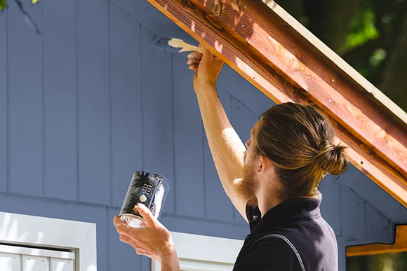 Person streicht Holzfassade mit Pinsel