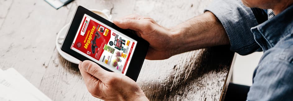 Eine Person schaut sich auf einem Tablet an einem Holztisch einen digitalen Prospekt an.