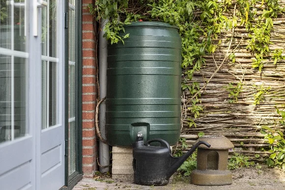 Grüne Regentonne mit Gießkanne