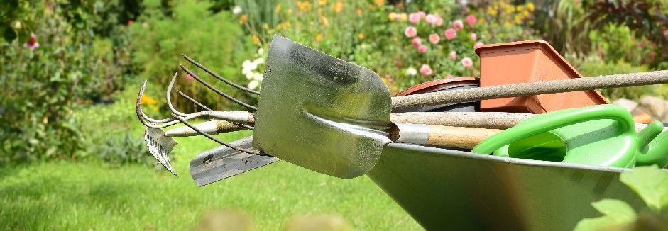 Diverse Gartenwerkzeuge in einer Schubkarre auf einer Wiese.