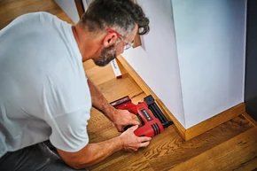 Person befestigt Holzleiste mit Druckluftnagler.