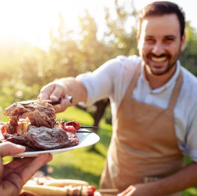 Person gibt Gegrilltes mit Grillzange auf Teller