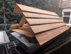 Hölzernes Vogelhaus mit Schnee auf einem Balkon.