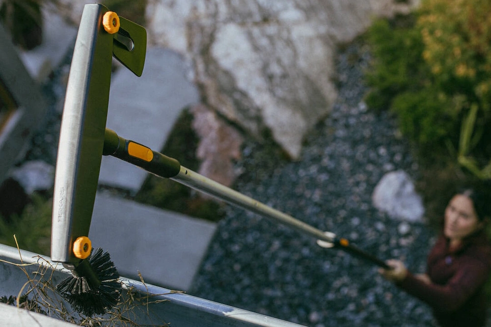 Eine Person reinigt eine Dachrinne mit einem Fiskars-Werkzeug