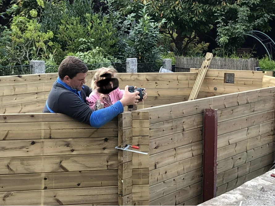 Person und Kind bauen Gartenhaus aus Holz