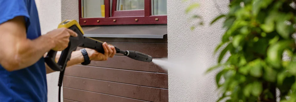 Person reinigt Hauswand mit Hochdruckreiniger