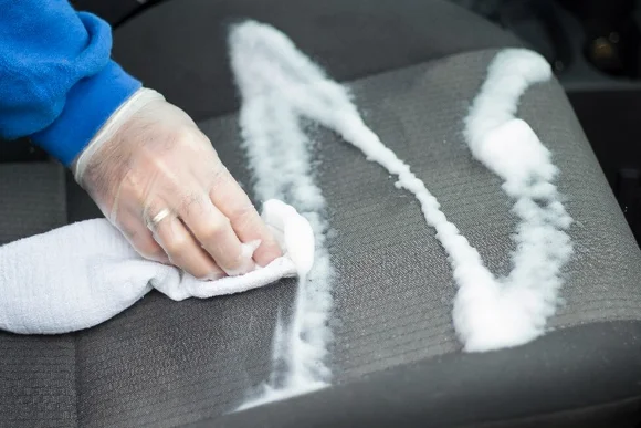 Person reinigt Autositz mit Tuch