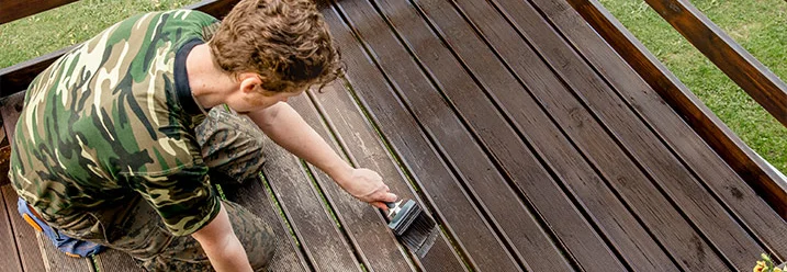 Person streicht Holzboden mit Pinsel