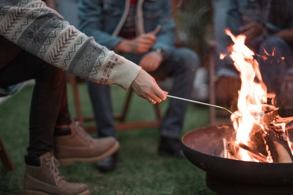 Eine Person röstet einen Marshmallow an einem Spieß über einer Feuerschale.