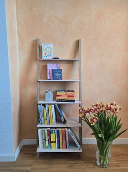 Ein Leiterregal mit Büchern steht neben einer Vase mit bunten Tulpen.