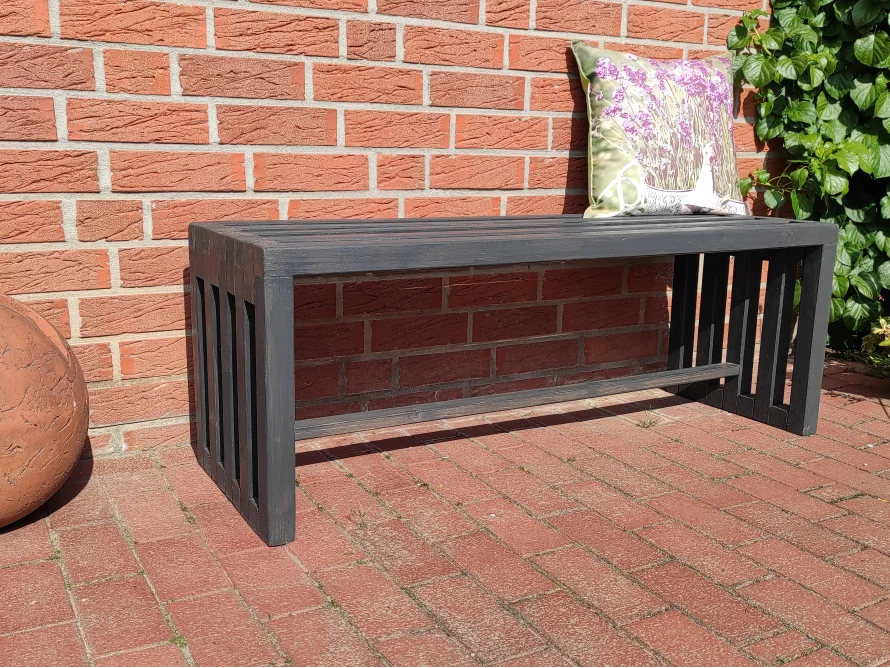 Schwarze Holzbank an einer Backsteinwand