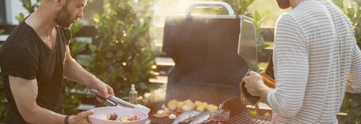 Zwei Personen grillen Fisch und Gemüse mit einer Grillzange.
