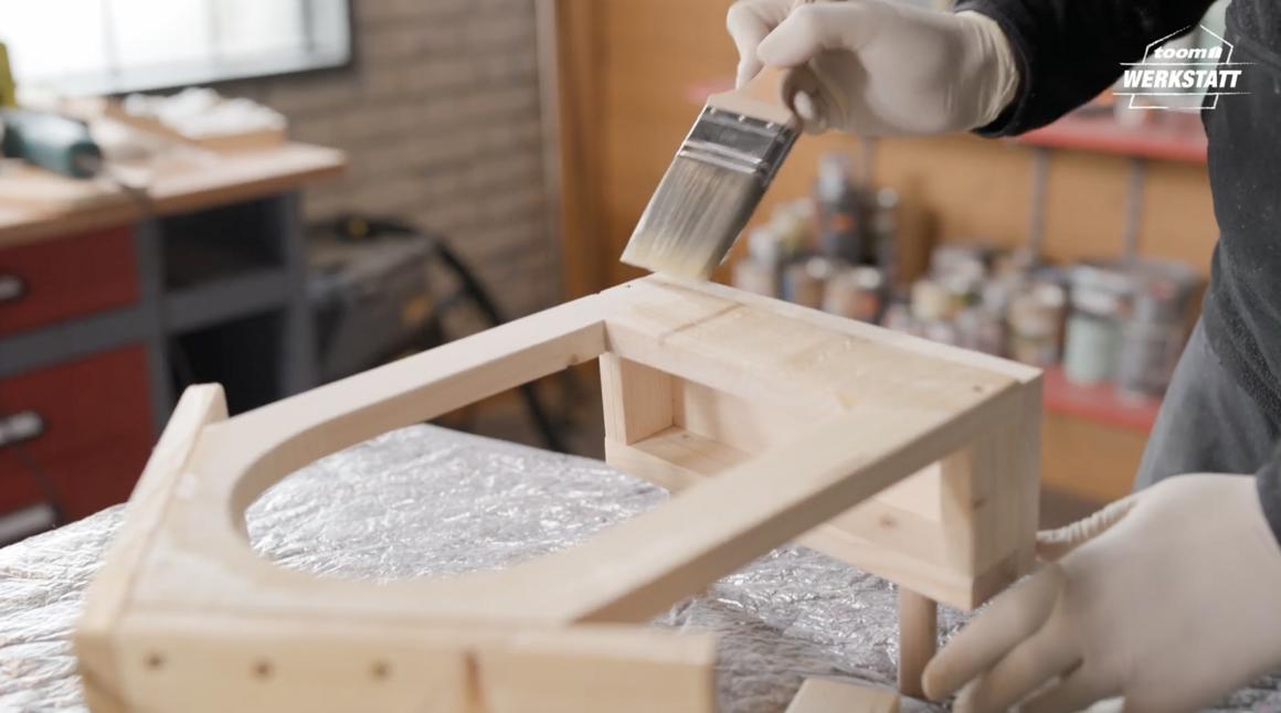 Person streicht Holz mit Pinsel