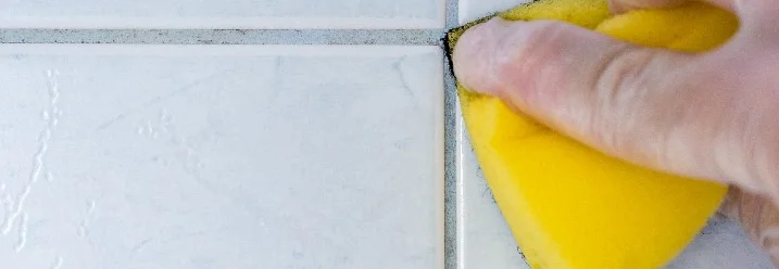 Hand reinigt Fliesenfugen mit Schwamm