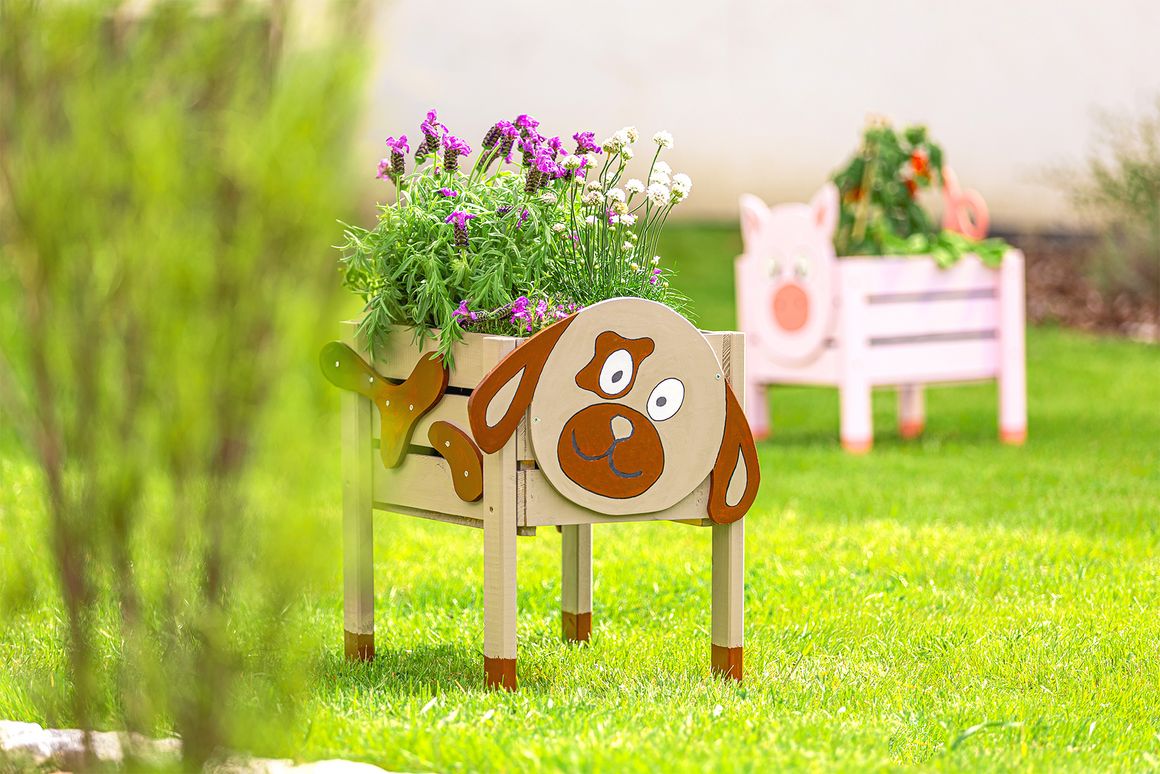 Ein bepflanzter Blumenkasten in Form eines Hundes steht auf einem Rasen.