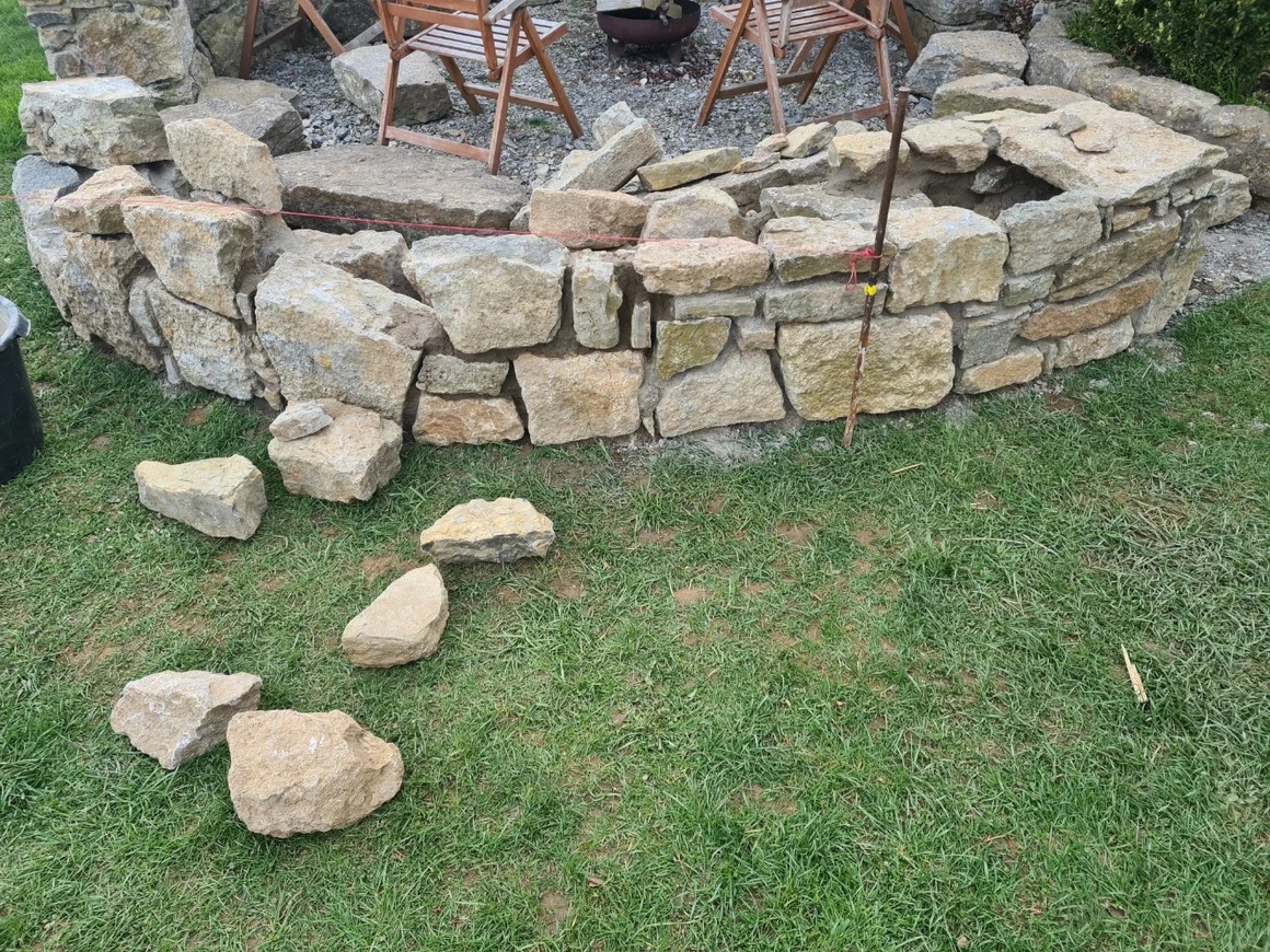 Eine runde Trockenmauer aus Natursteinen wird im Garten gebaut.