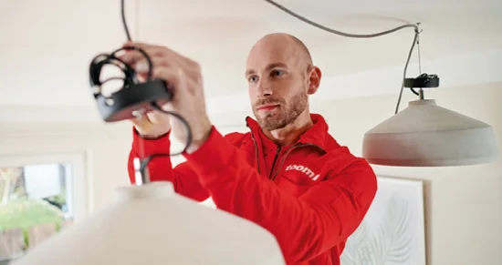 Eine Person in roter Arbeitskleidung montiert eine Deckenlampe.