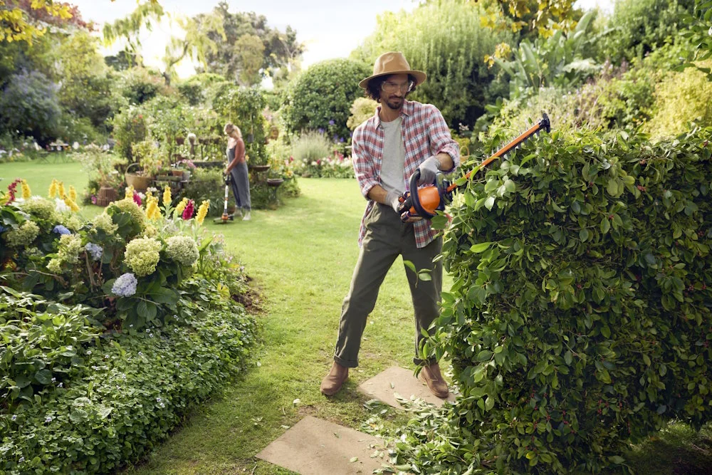 Person schneidet eine Hecke mit einer Heckenschere.