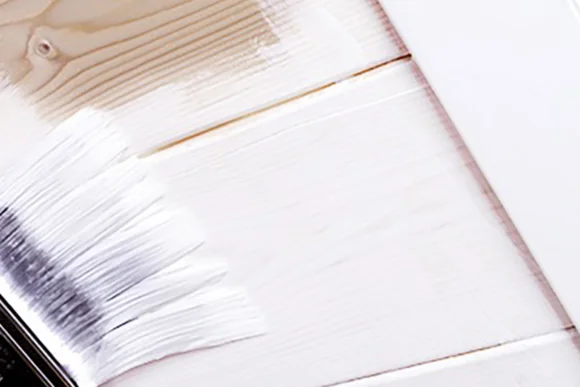 Pinsel trägt weiße Farbe auf Holz auf