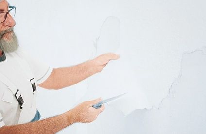 Ein Handwerker zieht große Stücke Tapete von einer Wand.