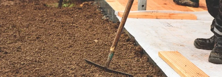 Person harkt Erde neben Holzterrasse