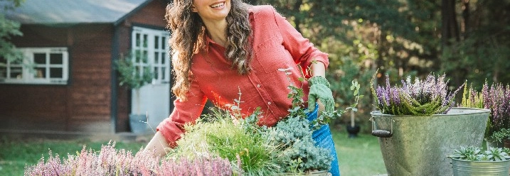 Lächelnde Person bei der Gartenarbeit mit Herbstpflanzen.