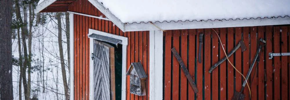 Ein roter Holzschuppen im Schnee mit Werkzeugen an der Wand.