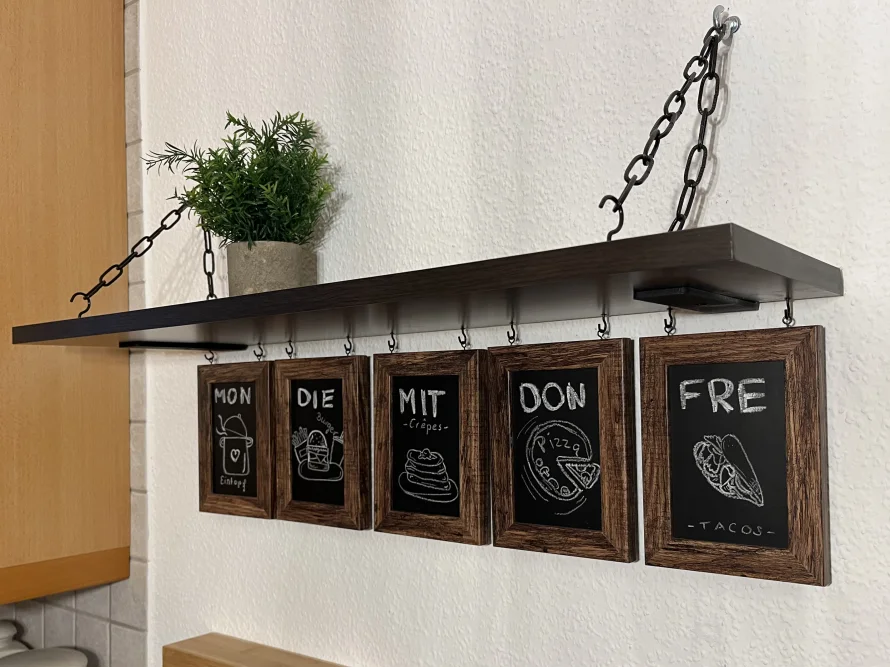 Kreativer Wochenplaner für Mahlzeiten an einem Hängeregal mit Tafeln.