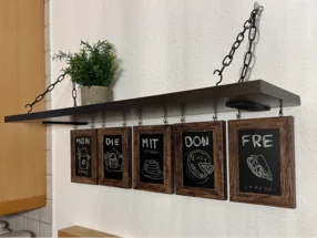 Kreativer Wochenplaner für Mahlzeiten an einem Hängeregal mit Tafeln.