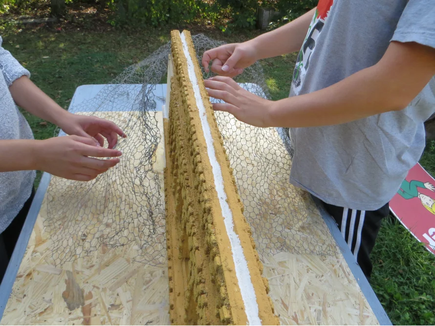 Zwei Personen bringen Maschendraht an einem Holzgerüst an.