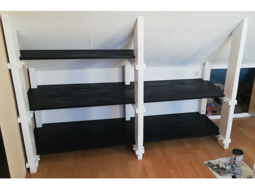 Ein weißes Regal mit schwarzen Brettern unter einer Dachschräge.