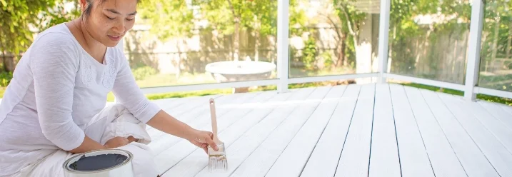 Person streicht Holzterrasse weiß
