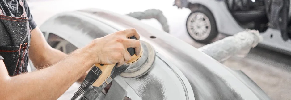 Person schleift Autoteil mit Schleifmaschine