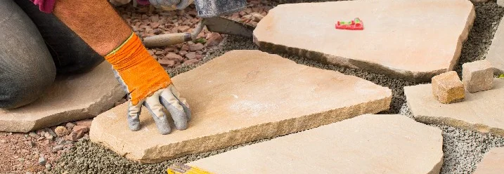 Person verlegt Steinplatten mit Gummihammer