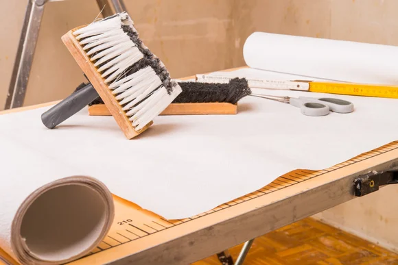 Tapete, Bürsten, Zollstock und Schere auf einem Tapeziertisch