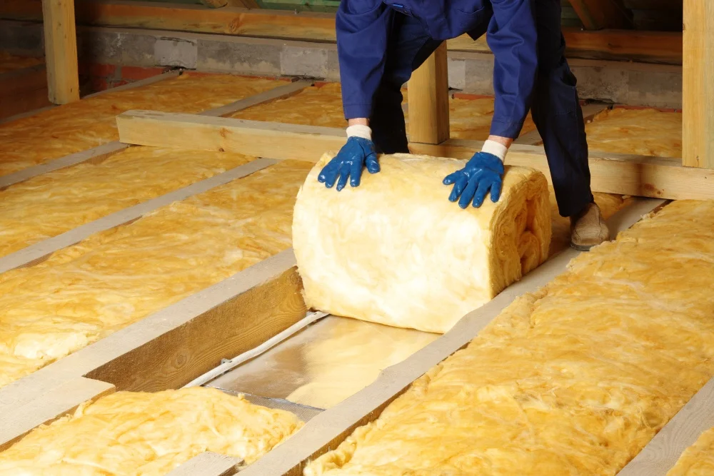 Eine Person dämmt den Dachboden mit gelber Dämmwolle.