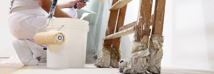 Person beim Streichen mit Farbrolle und Farbeimer