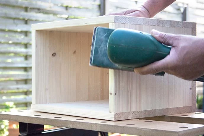 Person schleift Holzkiste mit Schleifgerät