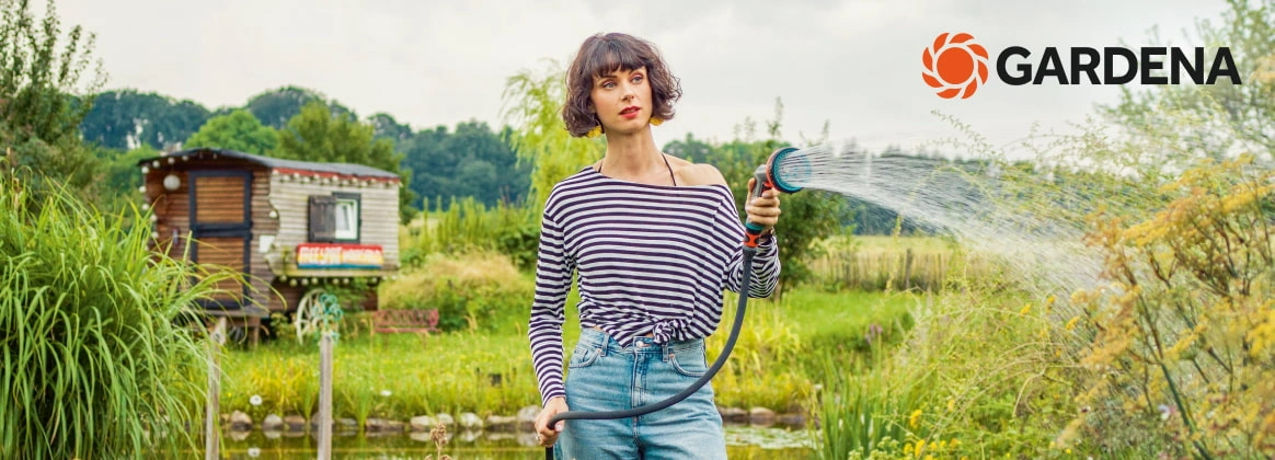 Eine Person steht mit einem GARDENA Schlauch in einem Garten