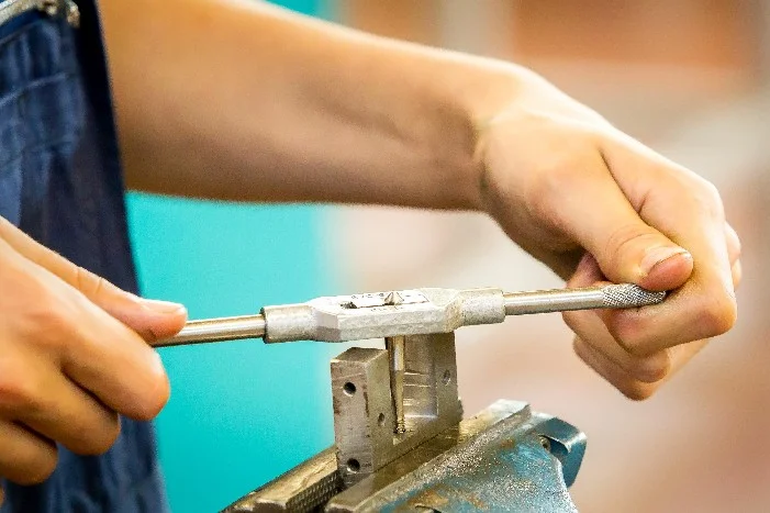 Person schneidet mit Schneideisen Gewinde.