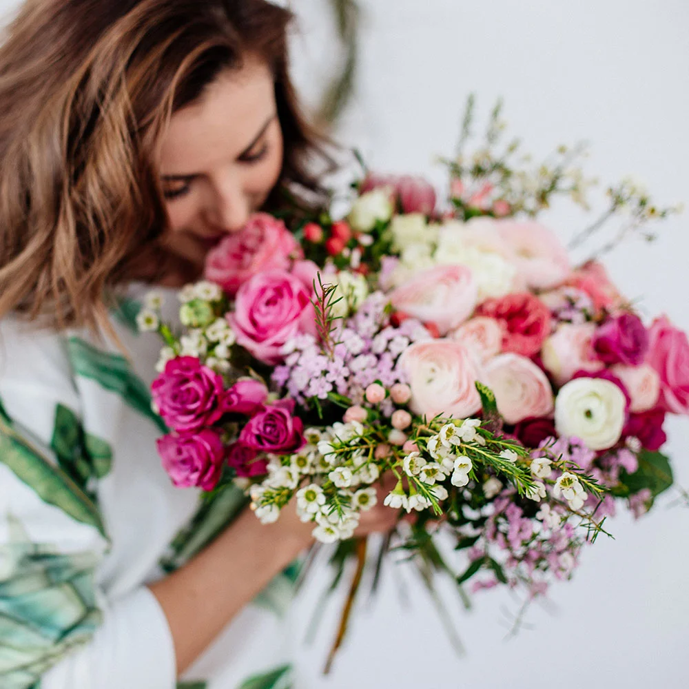 Person riecht an einem bunten Blumenstrauß