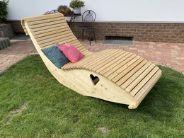 Eine geschwungene Holzliege mit Herz-Ausschnitt steht im Garten.