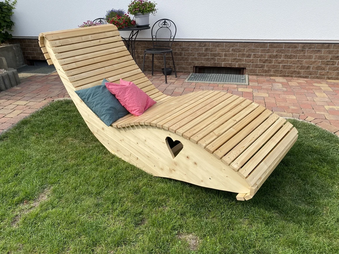 Eine geschwungene Holzliege mit Herz-Ausschnitt steht im Garten.