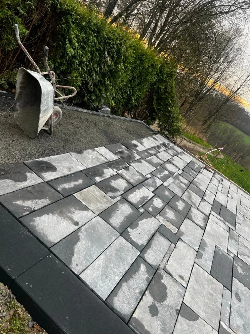 Eine im Bau befindliche Terrasse mit grauen Steinplatten und einer Schubkarre.