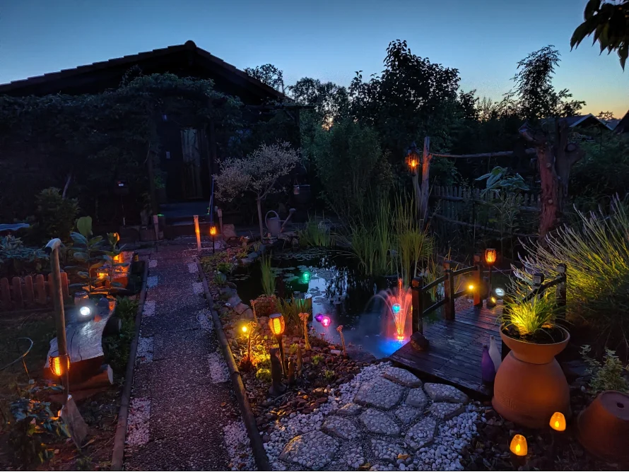 Beleuchteter Gartenweg mit Teich in der Dämmerung