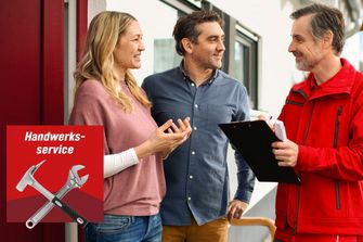 Ein Handwerker in roter Jacke berät ein Paar vor einem Haus.